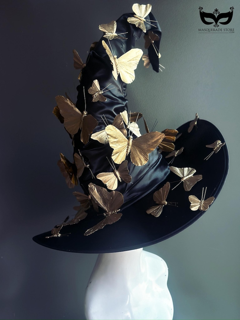 May include: A black witch hat adorned with numerous gold-colored butterfly decorations. The hat has a wide brim and a tall, pointed crown. The butterflies are of varying sizes and are attached to the hat with thin wires. The hat is displayed on a white mannequin head.