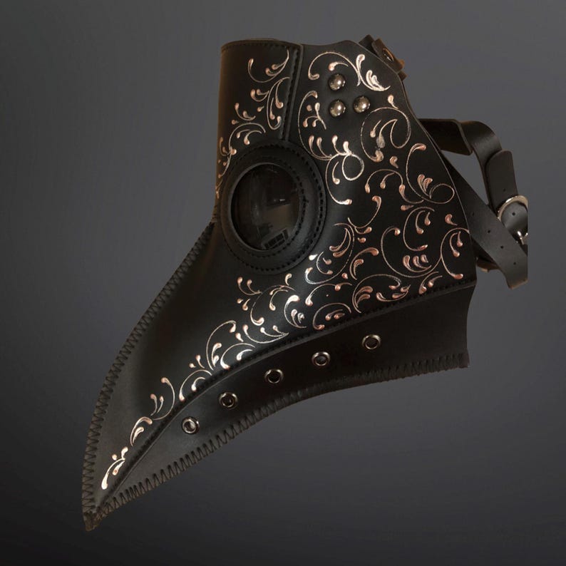 May include: A black leather plague doctor mask with a silver floral design and a clear eye piece. The mask has a long beak and is secured with a leather strap.
