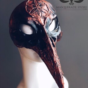 Pu&ograve; includere: Una maschera per il carnevale realizzata su misura con un lungo becco appuntito e una finitura color rame. La maschera ha un design circolare sulla fronte con una maschera per gli occhi nera.