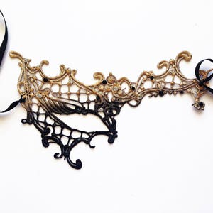 May include: A black and gold lace masquerade mask with a delicate design and black ribbon ties.