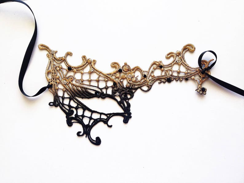 May include: A black and gold lace masquerade mask with a delicate design and black ribbon ties.