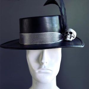 May include: Black hat with a silver ribbon, a skull, and a feather. The hat is displayed on a white mannequin head. The Masquerade Store logo is in the upper left corner.