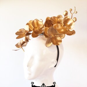 May include: Gold orchid flower headband with a black elastic band. The headband is decorated with multiple gold orchid flowers.