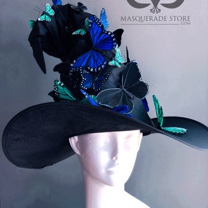 Pu&ograve; includere: Un cappello da strega nero con un'ampia tesa e una corona alta decorata con ornamenti a forma di farfalla blu e verde. Il cappello &egrave; su una testa di manichino bianca. MASQUERADE STORE .COM &egrave; stampato sullo sfondo.