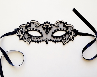 Könnte beinhalten: Eine schwarze Maskenballmaske aus Spitze mit Strasssteinen und einem schwarzen Satinband.
