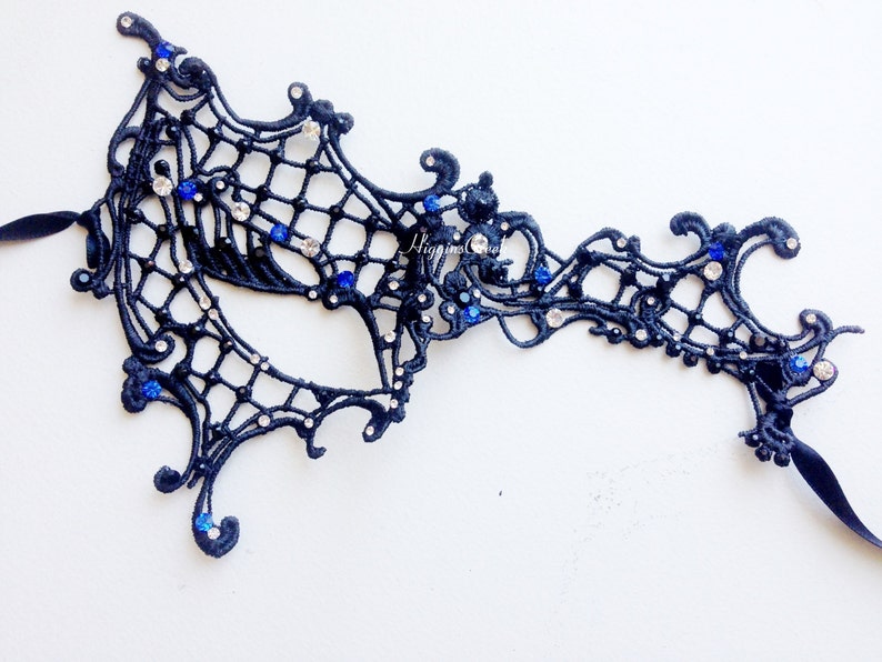 May include: A black lace masquerade mask with blue and clear rhinestones. The mask has a delicate, intricate design and is perfect for a costume party or masquerade ball.