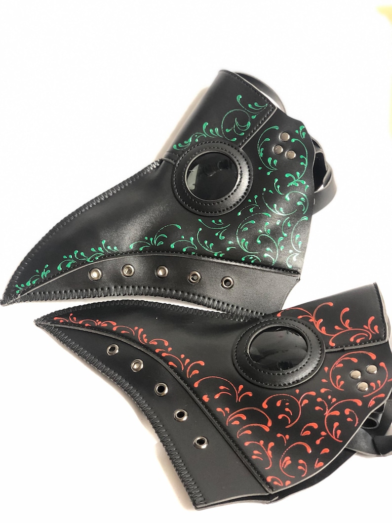 May include: Two black leather plague doctor masks with a decorative floral pattern. One mask has a green pattern and the other has a red pattern.