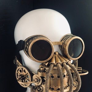 May include: Steampunk mask with brass-toned goggles and a detailed face covering. The mask features intricate gear and tube designs, creating a futuristic, industrial aesthetic. The goggles have dark lenses and a black elastic strap.