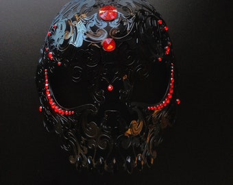May include: A black skull masquerade mask with intricate details and red rhinestone accents.