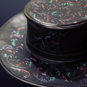 May include: A black leather hat with a wide brim and a crown decorated with a floral pattern in red, green, and silver.