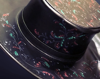 Puede incluir: Un sombrero de cuero negro con ala ancha y corona decorada con un diseño floral en rojo y verde.