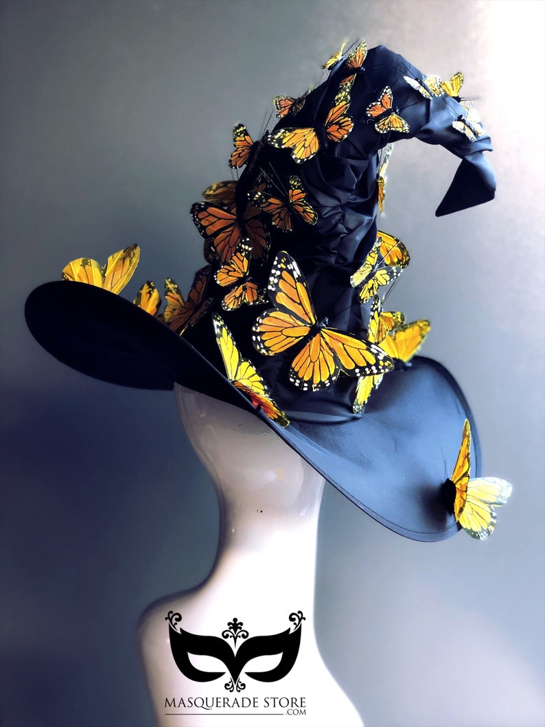 Pu&ograve; includere: Un cappello da strega nero con una corona alta e appuntita decorata con numerosi accenti di farfalle gialle e arancioni. Il cappello &egrave; esposto su un manichino bianco.