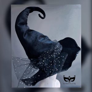 May include: A black witch hat with a curved tip and a wide brim. The hat is adorned with a sheer, dotted fabric and a bow. The Masquerade Store logo is visible in the bottom right corner. This hat is perfect for Halloween or costume parties.