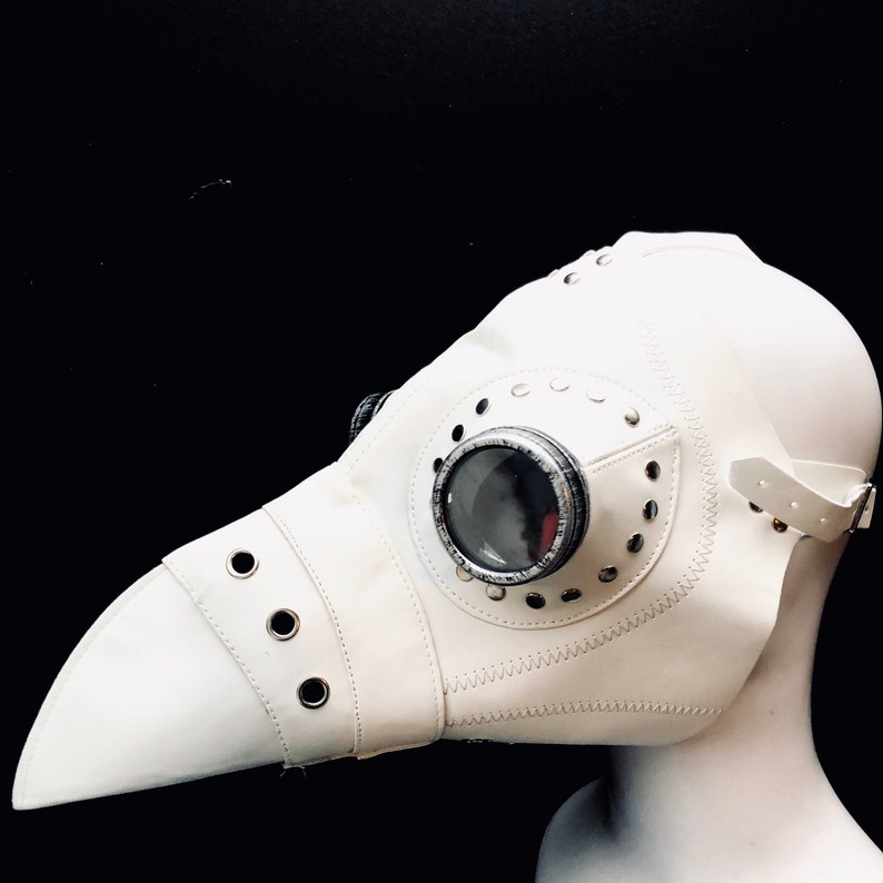 Pode incluir: M&aacute;scara de m&eacute;dico da peste de couro branco com uma pe&ccedil;a ocular redonda e transparente e um bico longo e pontiagudo. A m&aacute;scara tem uma correia para prend&ecirc;-la &agrave; cabe&ccedil;a.