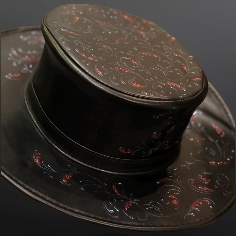 May include: A black leather top hat with a wide brim and intricate red and white floral designs.