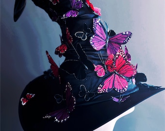 May include: A black witch hat with a tall, pointed crown adorned with pink and red butterflies. The hat is made of a soft, velvety fabric and has a wide brim.