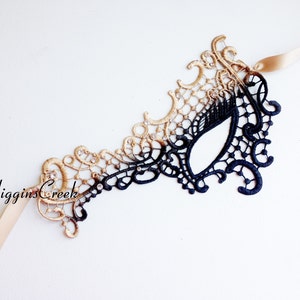 Peut inclure: Un masque de bal masqu&eacute; en dentelle noire et dor&eacute;e avec un design d&eacute;licat. Le masque a un seul trou pour l'&oelig;il et est attach&eacute; &agrave; un ruban de satin.