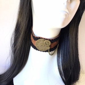 Op de afbeelding: Bruine leren choker met zwarte kanten rand en een gouden wijzerplaat met tandwielen.