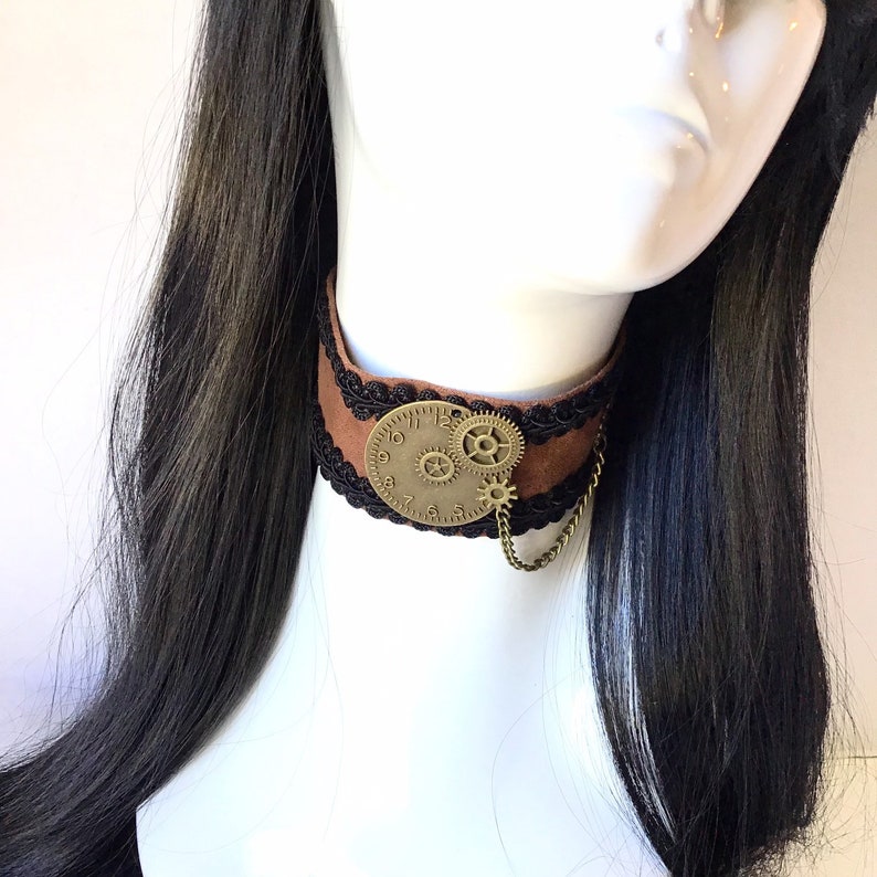 Op de afbeelding: Bruine leren choker met zwarte kanten rand en een gouden wijzerplaat met tandwielen.