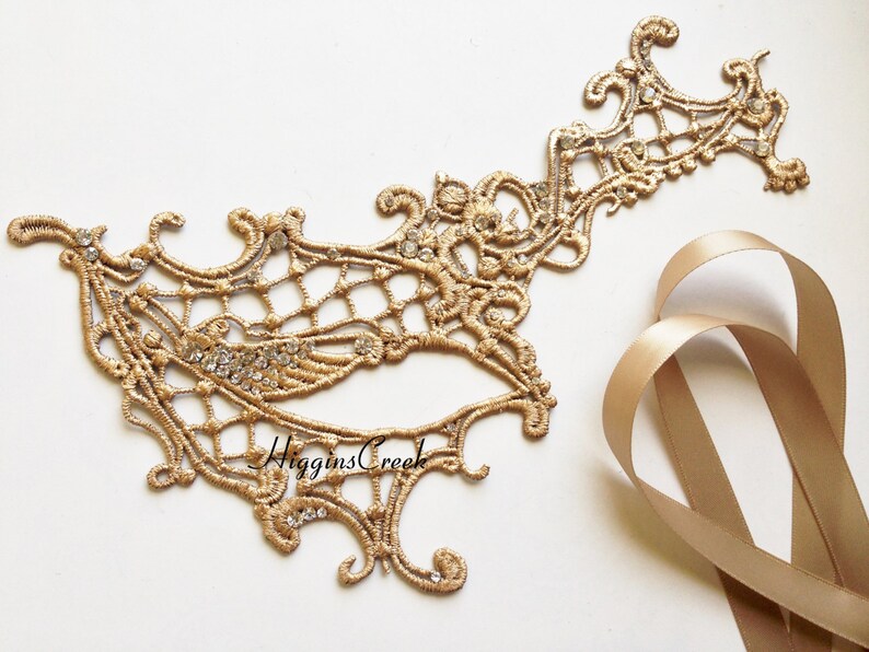 May include: Gold masquerade mask with intricate lace detailing and rhinestones. The mask is attached to a gold satin ribbon.