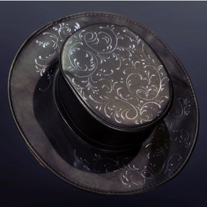Puede incluir: Un sombrero fedora negro con un dise&ntilde;o floral plateado. El sombrero tiene una ala ancha y una copa alta.