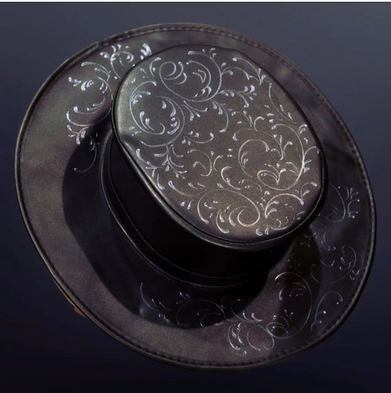 Puede incluir: Un sombrero fedora negro con un dise&ntilde;o floral plateado. El sombrero tiene una ala ancha y una copa alta.