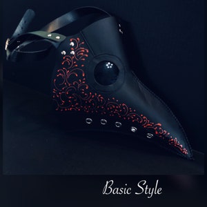 Pode incluir: Uma m&aacute;scara de m&eacute;dico da peste em couro preto com detalhes florais vermelhos e rebites prateados. A m&aacute;scara apresenta um bico longo, orif&iacute;cios para os olhos e correias ajust&aacute;veis. O texto "Basic Style" est&aacute; na parte inferior.