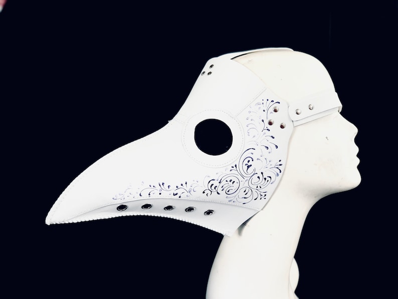 Puede incluir: M&aacute;scara blanca de m&eacute;dico de la peste con un dise&ntilde;o floral detallado y agujeros para los ojos. La m&aacute;scara est&aacute; hecha de cuero y tiene un pico largo.
