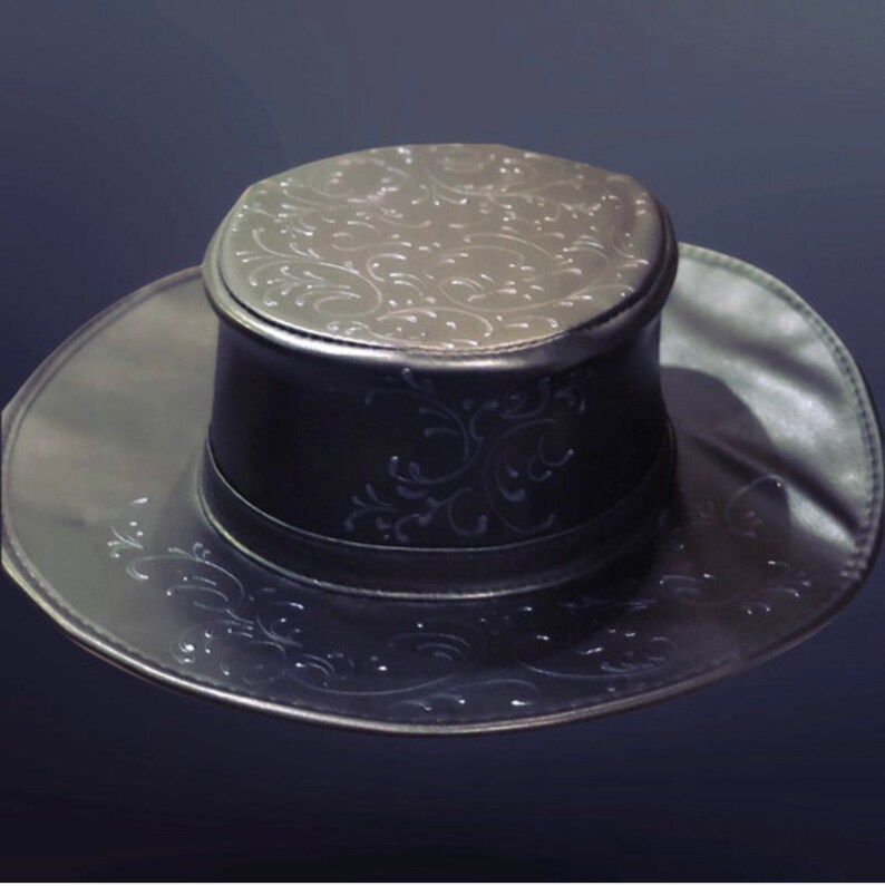 Puede incluir: Un sombrero de cuero negro con ala ancha y copa alta. El sombrero tiene un patr&oacute;n floral decorativo en relieve en la copa y el ala.