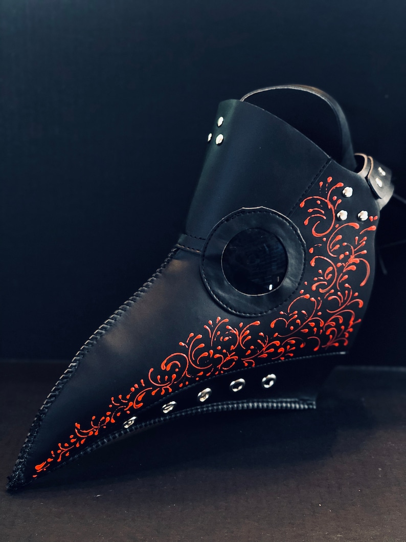 May include: A black leather plague doctor mask with red floral detailing and silver rivets.