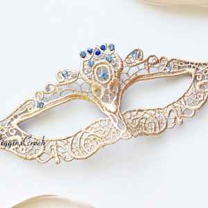 May include: Gold lace masquerade mask with blue and clear rhinestones. The mask has a delicate design and is tied with a satin ribbon.