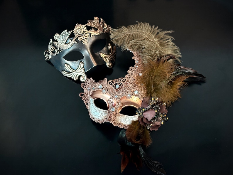 May include: Two masquerade masks, one black with gold accents and the other gold with brown lace and feathers.