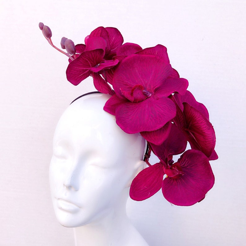 May include: A fuchsia orchid headband with multiple flowers arranged in a cascading design. The headband is worn on a white mannequin head.