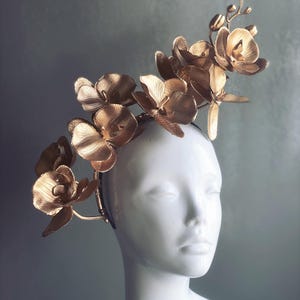 May include: A gold orchid headband with a delicate floral design. The headband is made of metal and features a series of orchid flowers that are arranged in a cascading pattern. The headband is perfect for adding a touch of elegance to any outfit.