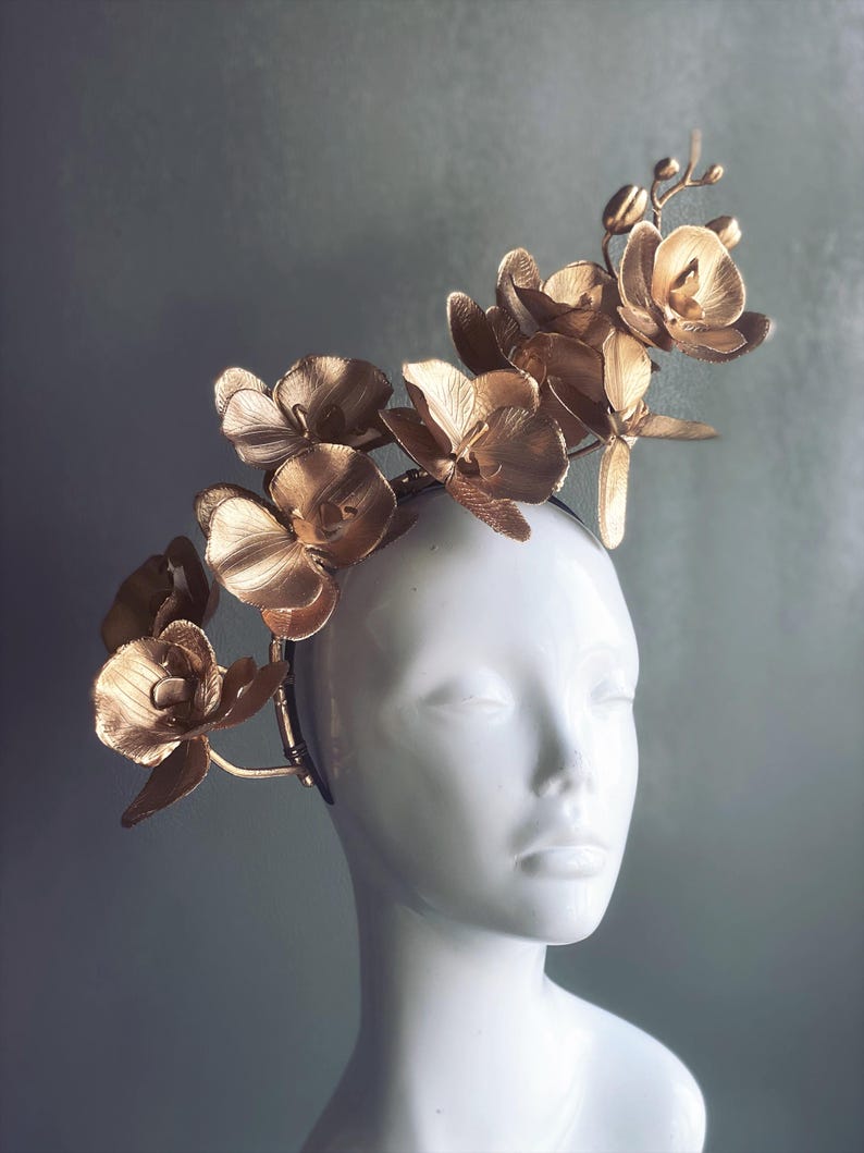 May include: A gold orchid headband with a delicate floral design. The headband is made of metal and features a series of orchid flowers that are arranged in a cascading pattern. The headband is perfect for adding a touch of elegance to any outfit.