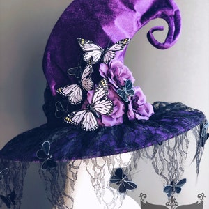 May include: Purple velvet witch hat with a black lace brim and a curled brim. The hat is decorated with purple flowers and white butterflies.