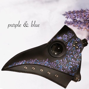 May include: A black leather plague doctor mask with a purple and blue floral design. The mask has a large round eye piece and a long beak.