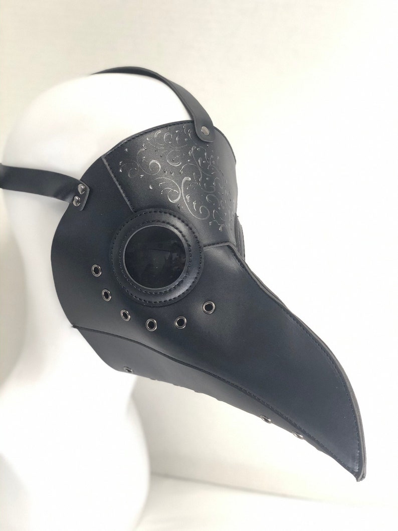 May include: Black leather plague doctor mask with a long beak and eye holes. The mask has a decorative floral pattern and metal eyelets.