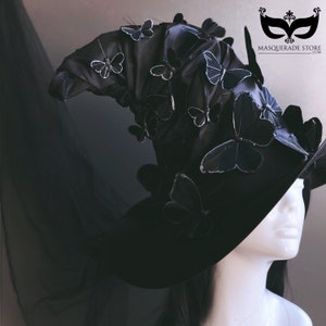 Puede incluir: Un sombrero de bruja negro con un ala ancha y una corona alta y puntiaguda. El sombrero está decorado con numerosas mariposas negras con detalles plateados. El sombrero lo lleva puesto un maniquí con el pelo negro.