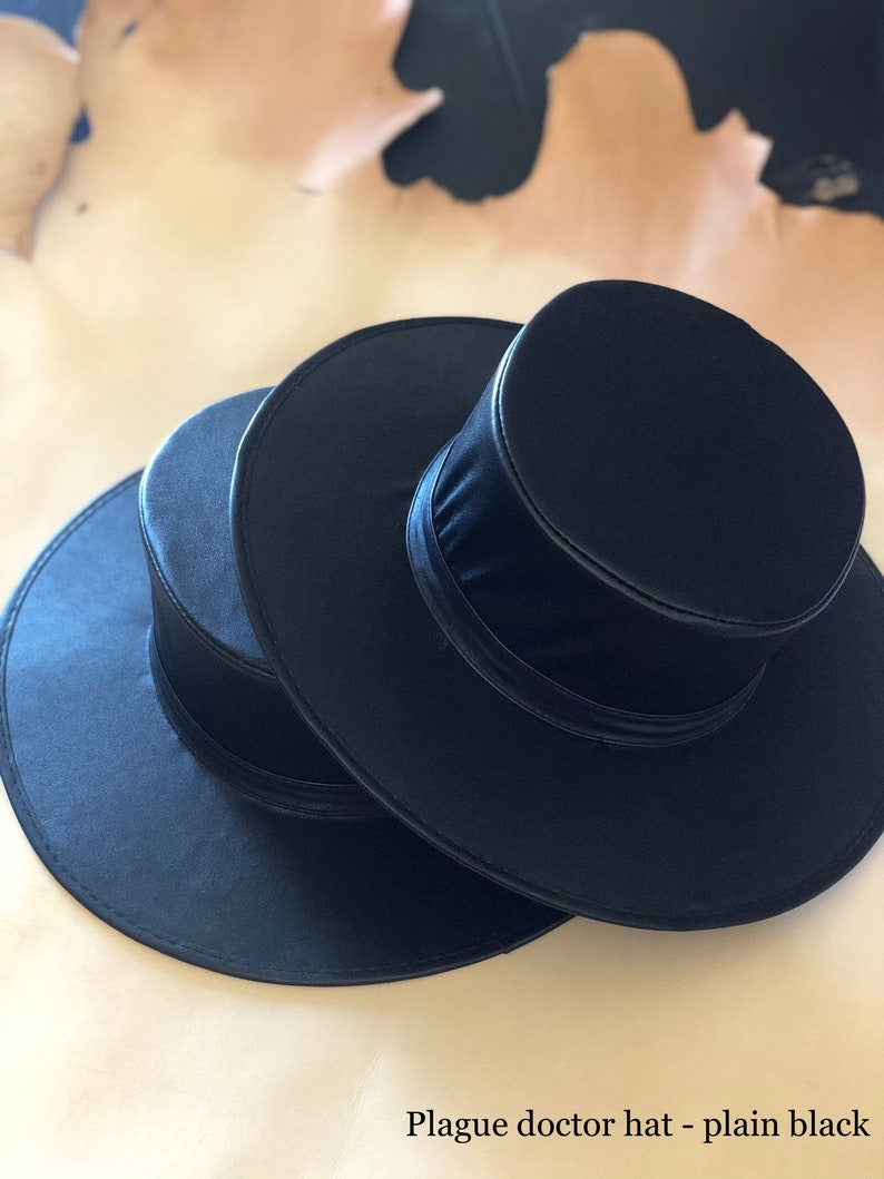 May include: Three plain black plague doctor hats are stacked, showcasing their round crowns and wide brims. The hats are made of a smooth, dark material, with a subtle sheen. The text "Plague doctor hat - plain black" is at the bottom.