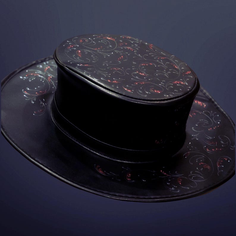 May include: A black leather hat with a wide brim and a tall crown. The hat is decorated with a red and white floral pattern.