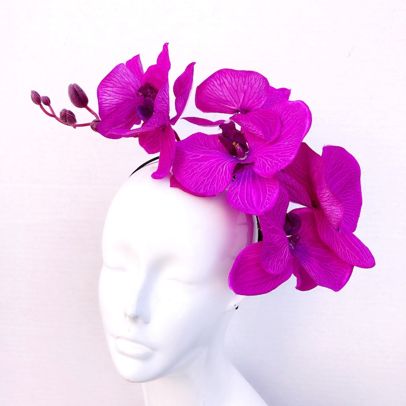 May include: A pink orchid flower headband with a black band. The headband is worn on a white mannequin head.
