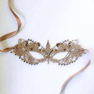 May include: A gold lace masquerade mask with beaded accents and a matching satin ribbon.