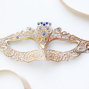 May include: Gold lace masquerade mask with blue and clear rhinestones. The mask has a delicate, intricate design and is tied with a satin ribbon.