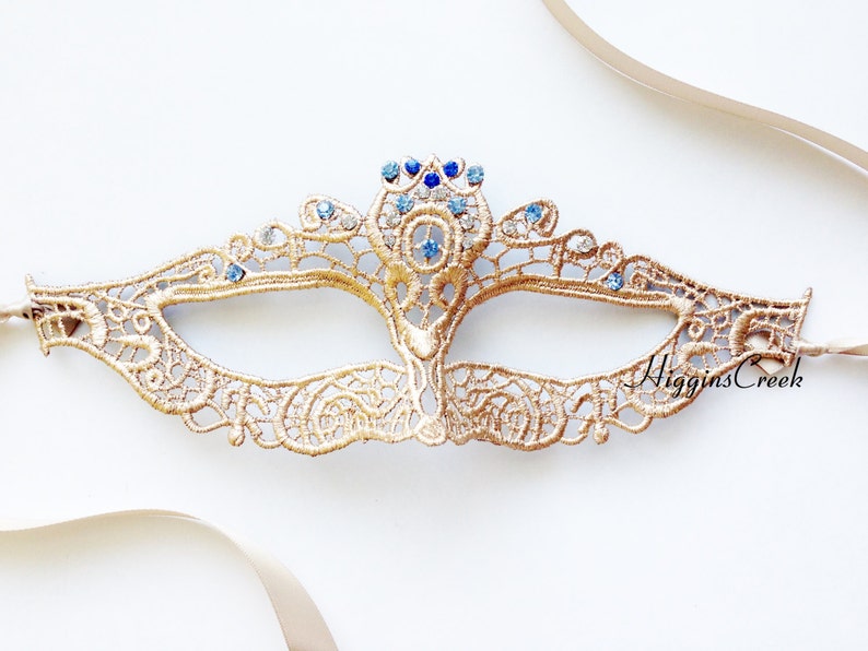 May include: Gold lace masquerade mask with blue and clear rhinestones. The mask has a delicate, intricate design and is tied with a satin ribbon.