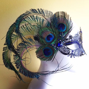 May include: A black and silver masquerade mask with blue and green peacock feathers. The mask has a delicate lace design and is adorned with rhinestones.