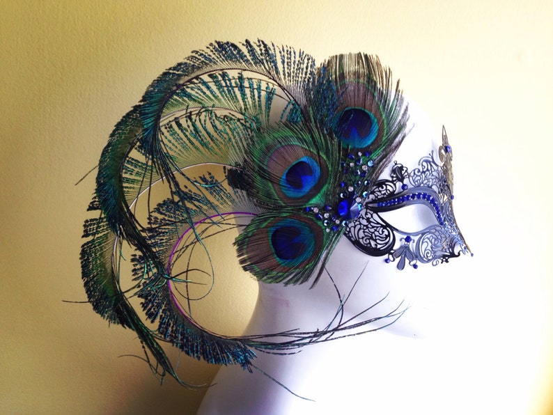 May include: A black and silver masquerade mask with blue and green peacock feathers. The mask has a delicate lace design and is adorned with rhinestones.