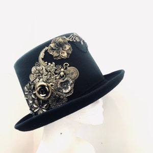 May include: A black top hat with a wide brim, adorned with gold-toned metal flowers, leaves, and a bee charm.
