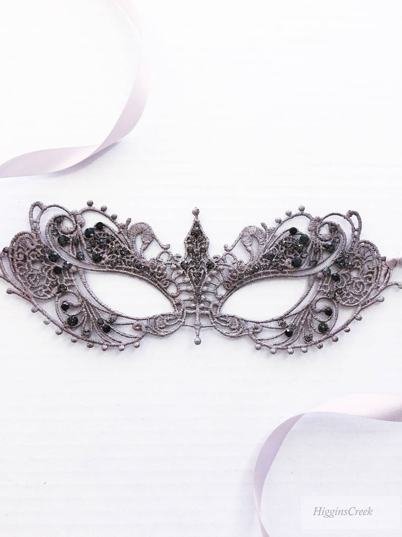 May include: A delicate, gray lace masquerade mask with black rhinestones. The mask has a delicate, intricate design and is perfect for a masquerade ball or costume party.