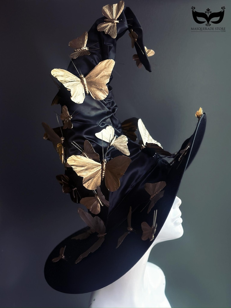 May include: A black witch hat adorned with numerous gold-colored butterfly embellishments. The hat has a wide brim and a tall, pointed crown. The butterflies are of varying sizes and are attached to the hat in a seemingly random pattern.